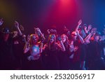 Costumed friends, boys and girls, attending Halloween party, celebrating with non-alcoholic drinks and treats, dancing and laughing. Night club event. Concept of Halloween, holiday, party, leisure