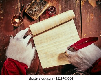 Costumed hands of Santa Claus writing a Christmas letter or greeting on a blank parchment scroll by candlelight on a vintage rustic table viewed from above - Powered by Shutterstock