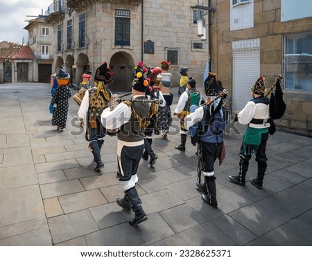 Costumed men drummers playing their drum and others playing their bagpipes in a folk band in procession in carnival masks down a street in the old town of Pontevedra at the August Pilgrim Festival