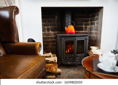 Cosy log burner in traditional English cottage. Organe kettle on fire and afternoon cream teas on table in foreground - Powered by Shutterstock