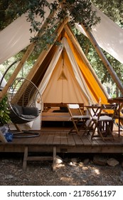 Cosy Tent In Istria, Rovinj Camping Site With Comfy Sofa On The Left, Table Set On The Right, Full Size Bed Inside And Plant Leafs In Foreground. Travel, Camp, Outdoor Tourism Concept.