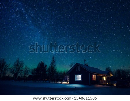 Cottage against the night sky with the Milky Way and the arctic Northern lights Aurora Borealis in snow winter Finland, Lapland