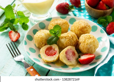 Cottage cheese dumplings with fresh strawberry, served with sour-honey sauce, delicious summer dessert on the kitchen wooden table. 