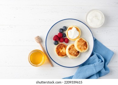 Cottage cheese fritters or syrniki served with berry fruits, greek yogurt and natural honey. Table top view, copy space for text or design elements - Powered by Shutterstock