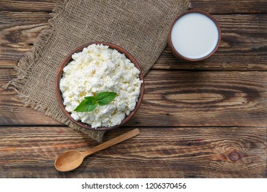 Cottage cheese and milk in clayware on wooden table, sackcloth table-napkin and wooden spoon