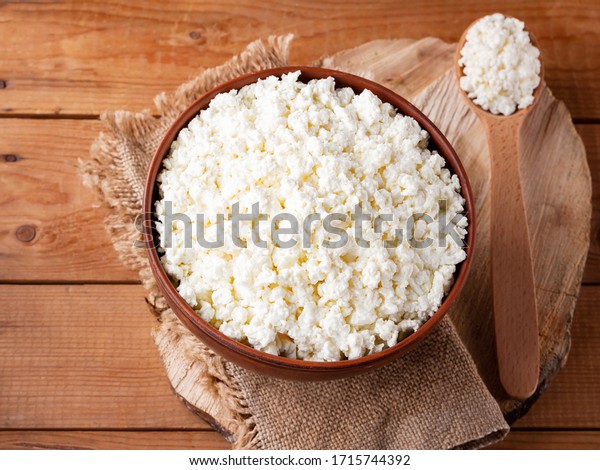 Cottage cheese on a\
wooden stand. Cottage cheese in a bowl. Soft cheese and wooden\
spoon on a wooden\
boards