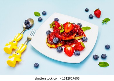 Cottage Cheese Pancakes With Fresh Berries And Strawberry Sauce. Healthy And Funny Breakfast Concept For Kids. Ripe Blueberry, Fragrant Mint Leaves, Cutlery. Gentle Blue Background, Close Up