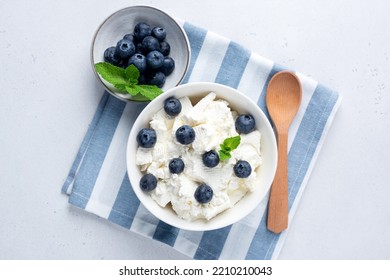 Cottage cheese, quark or curd in bowl served with blueberries on blue and white striped linen textile. Rich in calcium and protein dairy product, table top view