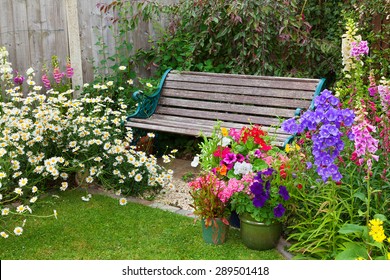 Cottage Garden With Wooden Bench And Flowers In Containers.