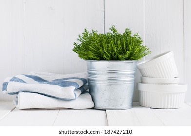 Cottage life, country kitchen decoration: a house plant in a metal pot, kitchen pottery, utensils and napkins on white painted board. Cozy home country life background is.