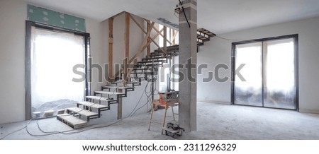 Cottage under construction. Interior unfinished house. Room with stairs leading to second floor. House under construction inside view. Renovation building. Room under construction with large windows