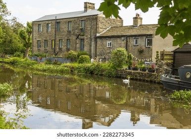Cottages converted from a Victorian Mill reflected in the waters of the Leeds and Liverpool Canal at Dowley Gap near Bingley - Shutterstock ID 2282273345