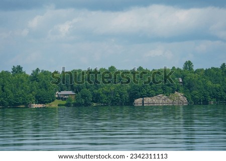 Cottages at the lake and a huge rock face jetting out of the water.  The rugged shoreline is beautiful.  rock,  giant,  steep, colourful, homes,  cottage on the rock, sky,  blue, green, Barry's Bay