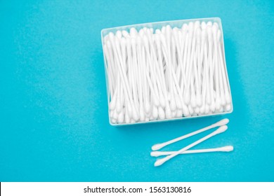 Cotton buds in plastic transparent rectangular container and several cotton buds separately on a blue background. Top view. Copy, empty space for text