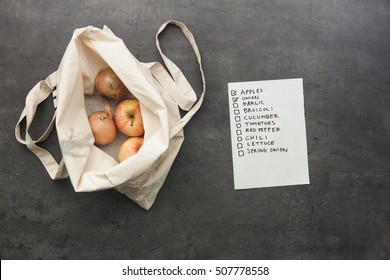 Cotton Shopping Bag With Onion And Apples Inside With Checked Shopping List. Flat Lay Food On Table.