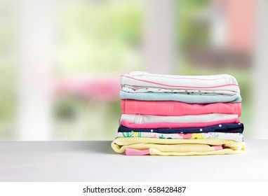 Cotton stack of colorful folded clothes on white table indoors empty space background.Household concept.Clean laundry pile.