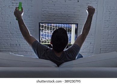 Couch Back View With Young Man Home Alone Watching Soccer Or Football Game In Television Enjoying And Celebrating Goal And Victory Holding Beer Bottle Gesturing On The Sofa Happy And Excited