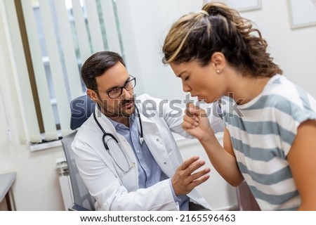 Coughing woman visiting doctor at clinic, patient coughing at medical appointment with her doctor. Sick woman visiting doctor at the hospital.