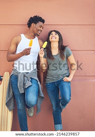 I could listen to you laugh all day. Shot of a happy young couple eating ice lollies together.