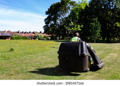 A Council Worker Riding On A Sit On Lawnmower Cutting The Grass In A Public Park On A Hot Summers Day