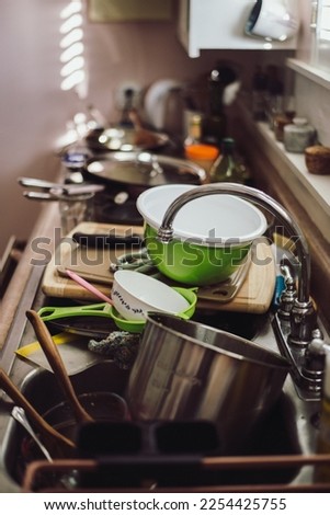 A counter and sink is filled to the brim with dirty dishes. The kitchen is cluttered with bowls, pans, and utensils that need washing.  ストックフォト © 