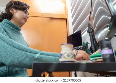 Counter View Of A Latina Woman Working At Her Desk At Home With Her Laptop Computer.