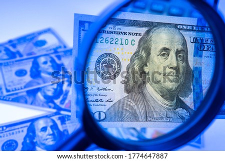 Counterfeit money. A hundred-dollar bill is studied with a magnifying glass. Money in the ultraviolet light. Concept - checking dollars for authenticity. Search for watermarks on banknotes. Fake