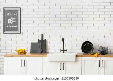 Counters with sink, black dinnerware, chopping boards and lemons near white brick wall