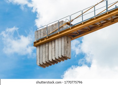 A counterweight of concrete blocks on the tail of a tower crane against a blue sky with clouds. Close-up