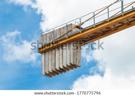 A counterweight of concrete blocks on the tail of a tower crane against a blue sky with clouds. Close-up