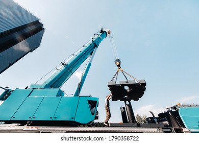 the counterweight is installed by an unrecognizable worker on a large blue car crane and is prepared to work on a site next to a large modern building. The largest truck crane for solving complex