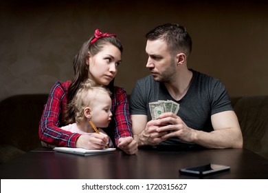 Counting Family Money. Husband And Wife Look At Each Other Seriously, A Little Daughter Sits On His Wife S Lap. Financial Difficulties In A Young Family, Crisis, Lack Of Money