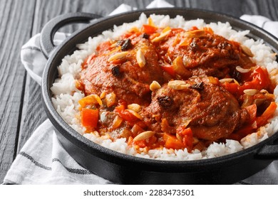 Country Captain chicken fried and then stewed with vegetables, raisins, almonds, tomato sauce and curry, served with rice in a pan on the table. Horizontal