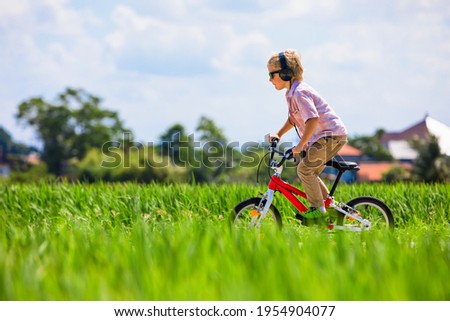 Country cycling walk. Young rider kid in headphones, sunglasses riding bicycle. Happy child have fun on field trail. Active family lifestyle, sports, outdoor recreational activities on summer holiday