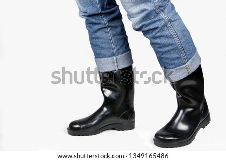 Country fashions style, blue jeans combined with shiny black rubber boots in front of a white background.