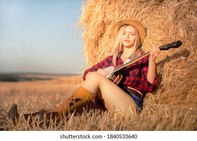 A Country Girl With A Banjo Sits In A Field Near Haystack .