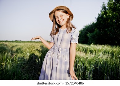 
A country girl in a straw hat and a vintage dress is standing in a field with green rye. Smiles
