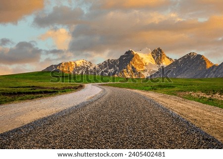 Country gravel road and green meadow with snow mountain natural landscape at sunset