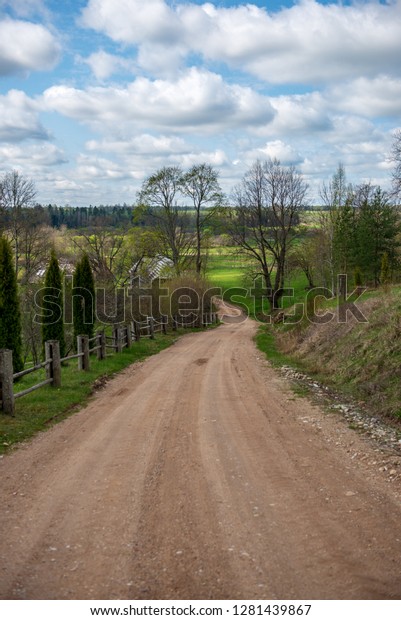country gravel road in\
perspective with old and broken asphalt in spring season with poor\
vegetation