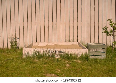 Country House Cottage, Backyard, White Wooden Fence Green Lawn And White Sandpit With Lettering And A Tank For Toys                               