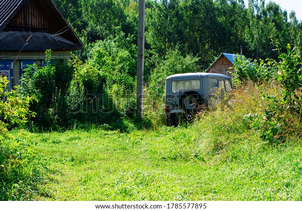 Country house in grass, bushes and trees. An old\
car SUV is parked near the\
house.