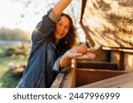 Country joy, woman with an egg in a country chicken coop. Cheerful homesteader showcases an egg at her countryside dwelling. Sustainable lifestyle, organic farmer