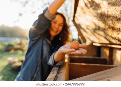 Country joy, woman with an egg in a country chicken coop. Cheerful homesteader showcases an egg at her countryside dwelling. Sustainable lifestyle, organic farmer - Powered by Shutterstock