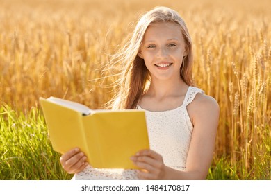 Land-, Literatur- und Freizeitkonzept - Lächelndes junges Mädchen in weißer Kleidung liest Buch über Getreidefelder im Sommer