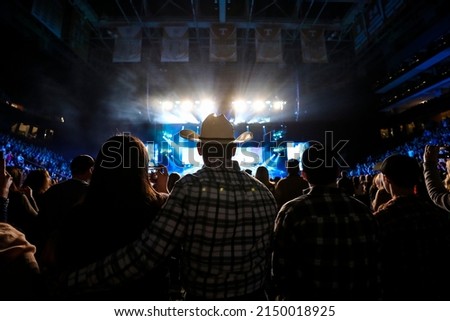 A country music fan watches a live concert wearing a cowboy hat.