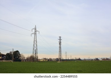 Country  road between fields with bare trees and electricity pylons with over head cables on a cloudy day