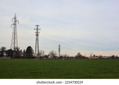 Country  road between fields with bare trees and electricity pylons with over head cables on a cloudy day