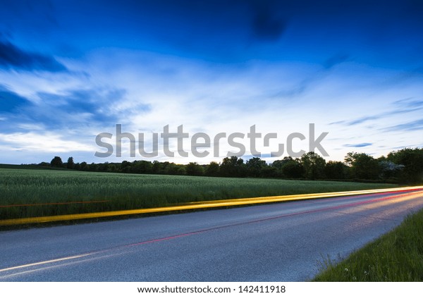 Country road with car\
light strips at dusk