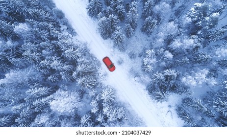 Country Road Going Through The Beautiful Snow Covered Forest. Red Car Driving On Winter Road. Aerial View. Drone Photography.