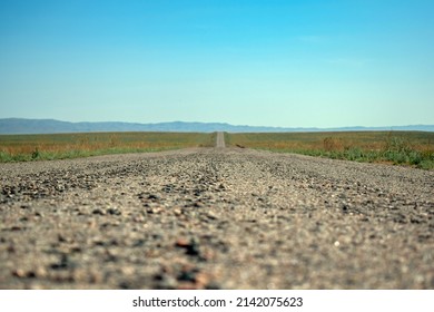 Country road from ground level in summer under clear blue sky - shallow depth of field, shot in the steppes of Kazakhstan. View of an old asphalt intercity road, bokeh foreground. Road closeup blur